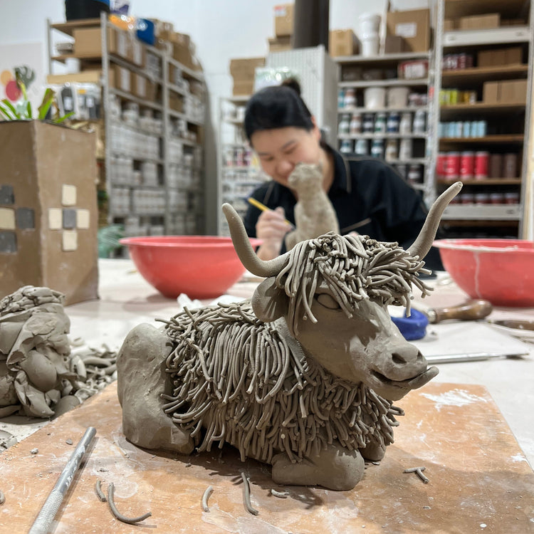 Clay sculpture of a horse head on a wooden surface with a person in the background.