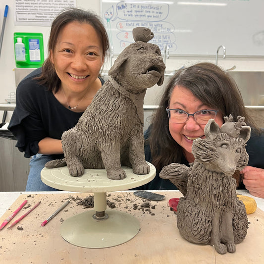 Two people posing with a ceramic sculpture of two animals on a table.